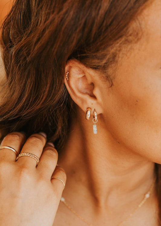 Close-up of a person wearing gold earrings and rings with a blurred background