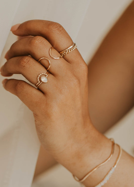 Close-up of a hand wearing gold rings and a bracelet on a blurred background