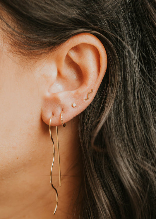 Close-up of an ear with gold earrings and dark hair.