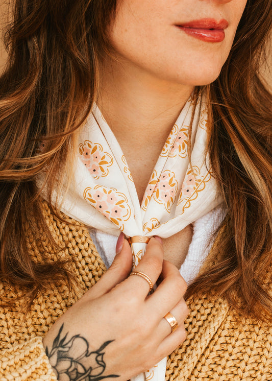 Woman wearing a beige knitted sweater and a white scarf with floral patterns.