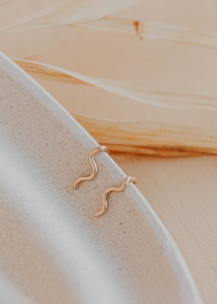 14k gold fill wavy ear climber earrings by Hello Adorn resting on a speckled ceramic dish
