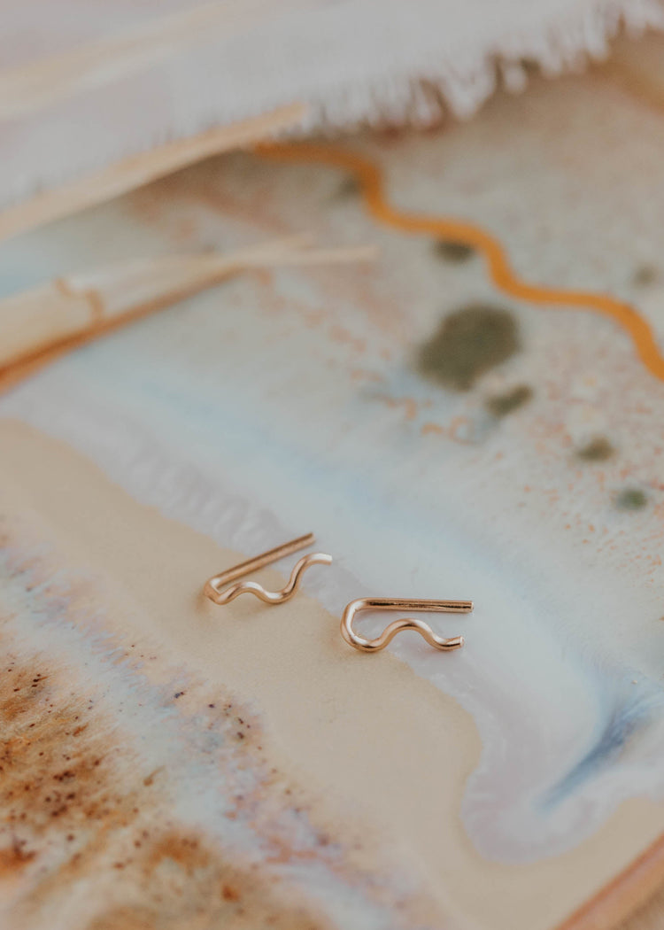 14k gold fill wavy ear climber earrings by Hello Adorn laid on an artistic ceramic tray