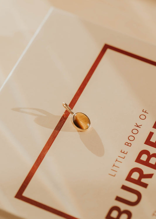 Gold tigers eye pendant sitting on a Burberry book