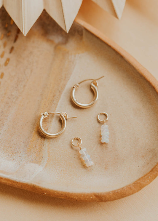Gold hoop earrings and a small stone charm on a textured beige surface.