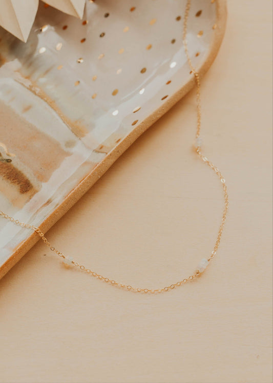 Gold necklace on a textured beige surface with a dish in the background