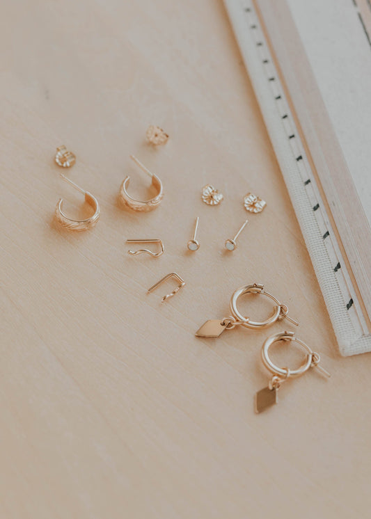 Collection of gold earrings on a beige surface with a ruler for scale.