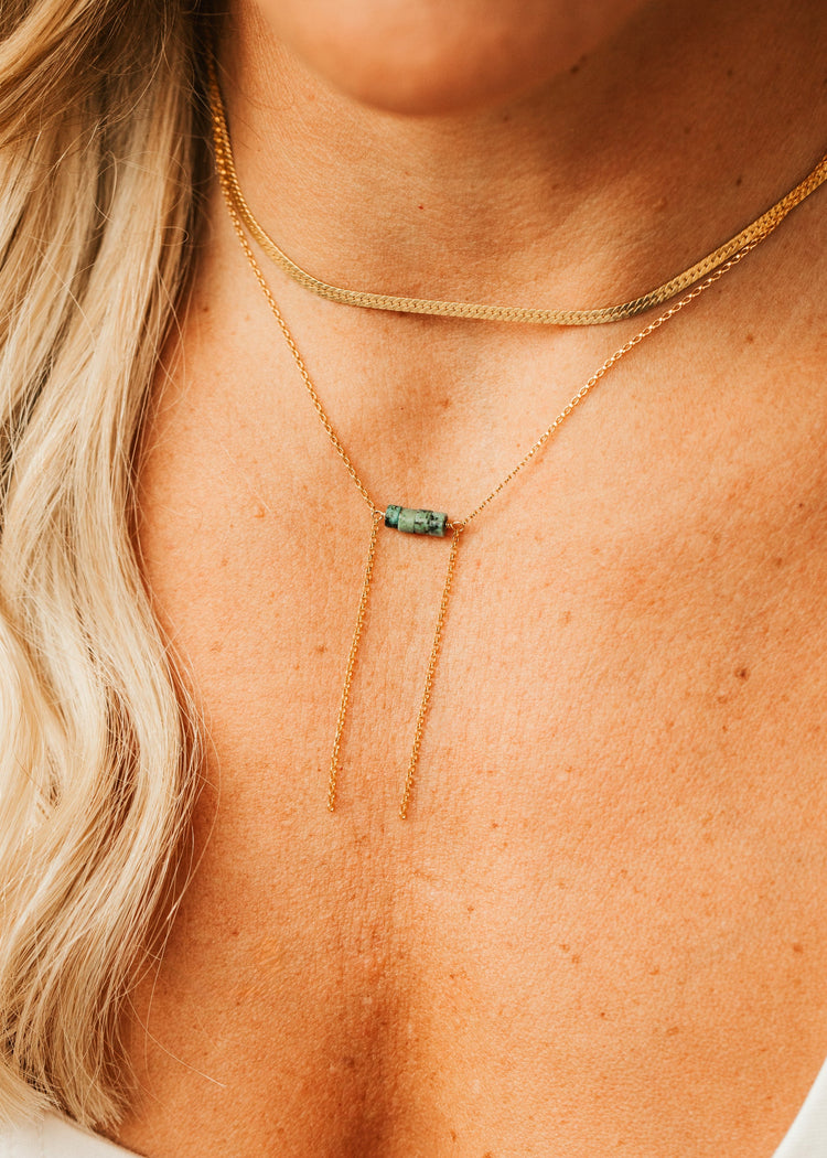 Close-up of a person wearing a gold necklace with a green gemstone on a white background