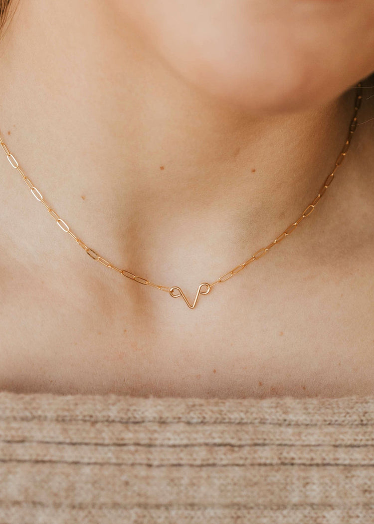 A close-up image of a woman wearing a gold chain necklace with a simple, uterus shaped pendant.