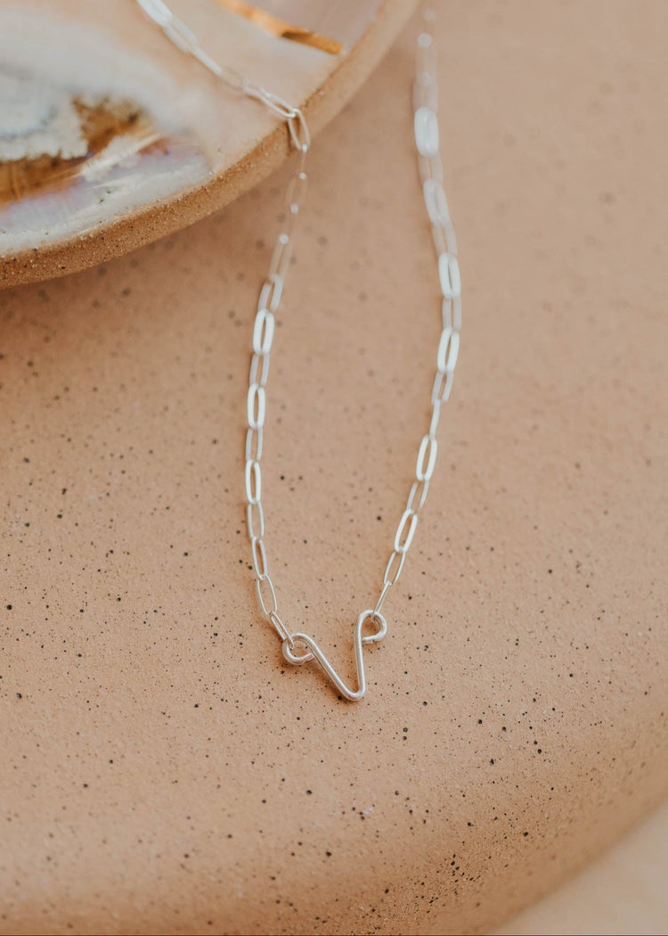 A gold-colored necklace with a simple, uterus pendant laid out on a light surface.
