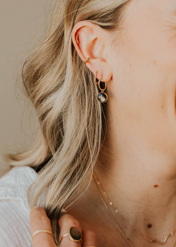 Close-up of a person wearing earrings and a necklace with a neutral background