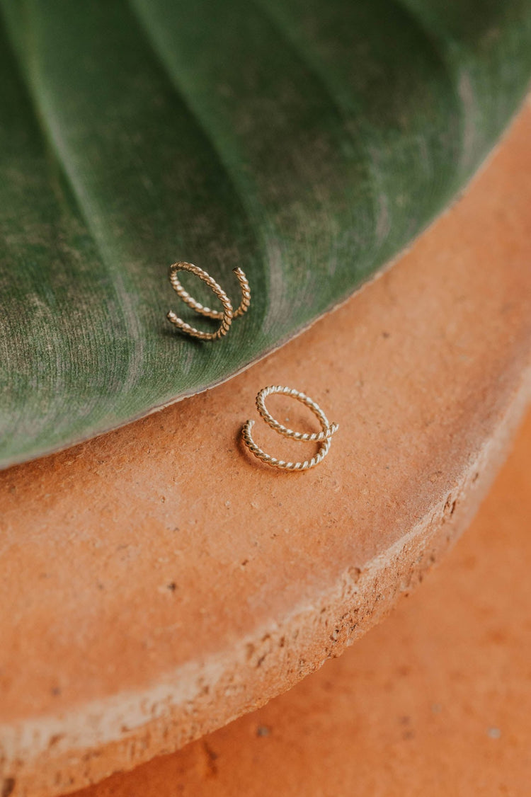 14k gold fill tiny twist earrings by Hello Adorn on a terracotta dish with tropical leaf