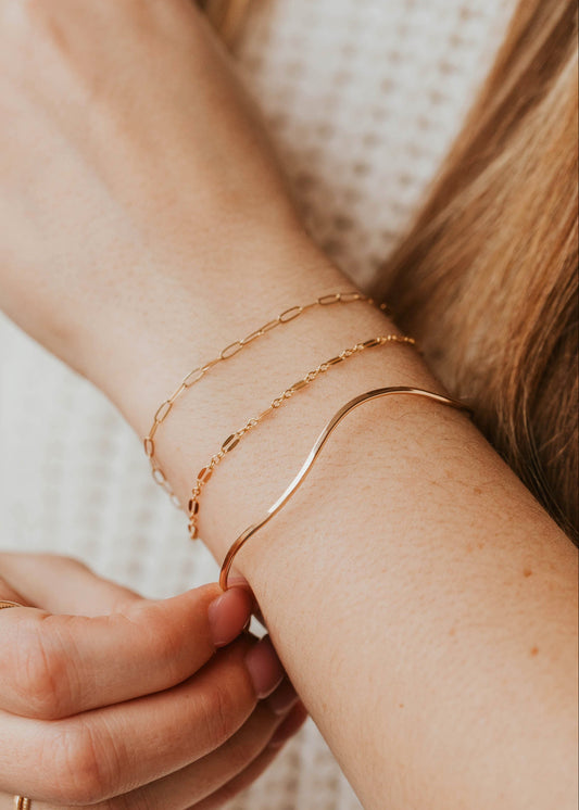 Close-up of a person's wrist with gold bracelets and rings on a neutral background
