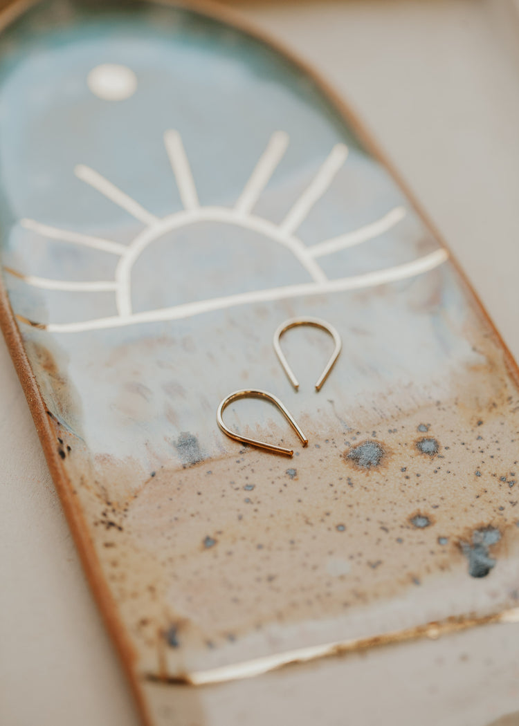 14k gold fill tiny horseshoe threader earrings by Hello Adorn laid flat on a sun design jewelry tray