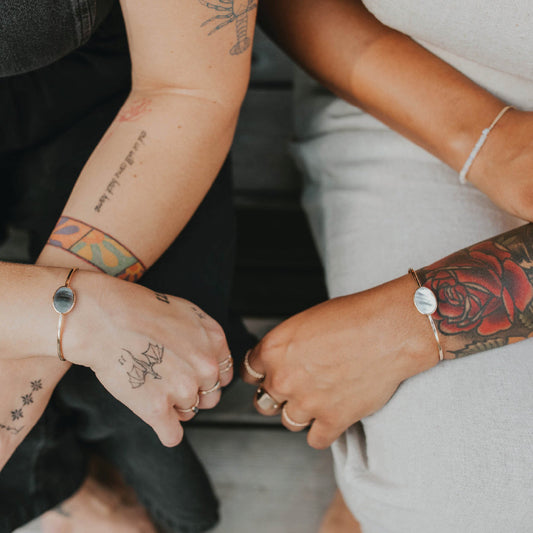 two arms feature cuff bracelets, one with a dark stone and one with a light stone