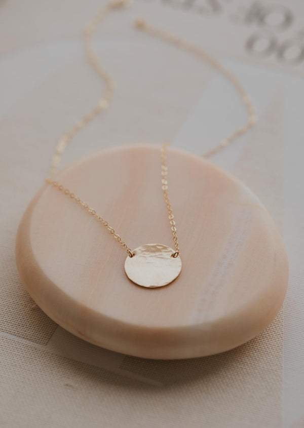A necklace with a circle pendant to create the Supermoon Necklace handmade by Hello Adorn using a gold disc necklace with a dainty chain necklace to create this moon statement necklace.