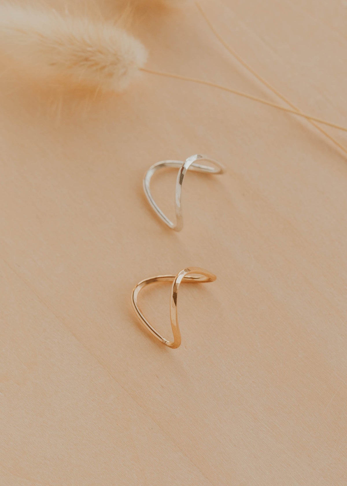 Two gold and silver hoop earrings on a beige background