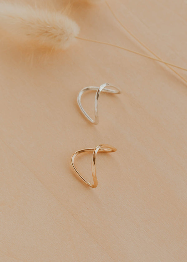 Two gold and silver hoop earrings on a beige background
