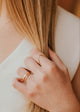Close-up of a hand with gold rings holding blonde hair, wearing a white top.