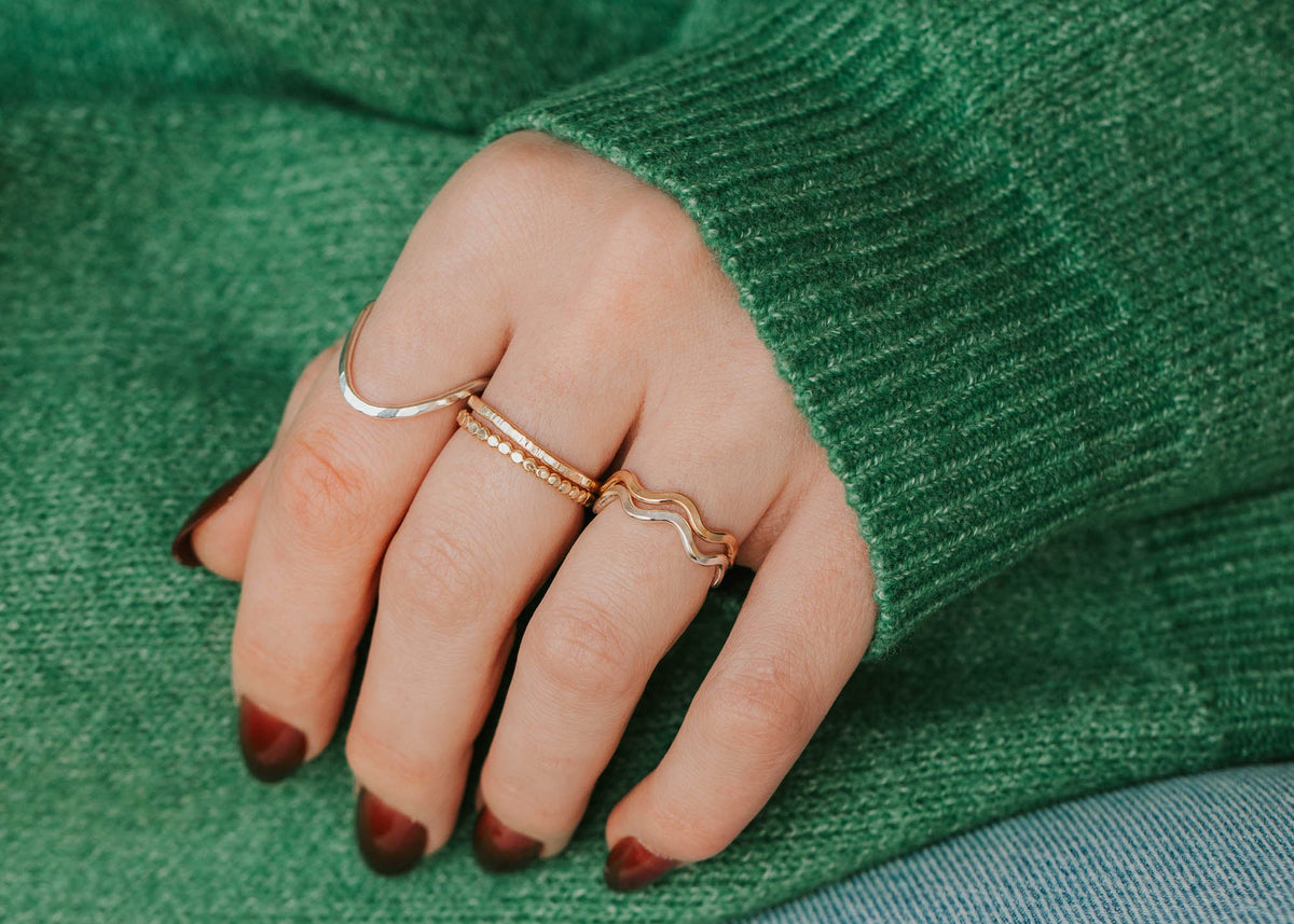 Close-up of a hand wearing gold rings on a green sweater and blue jeans background