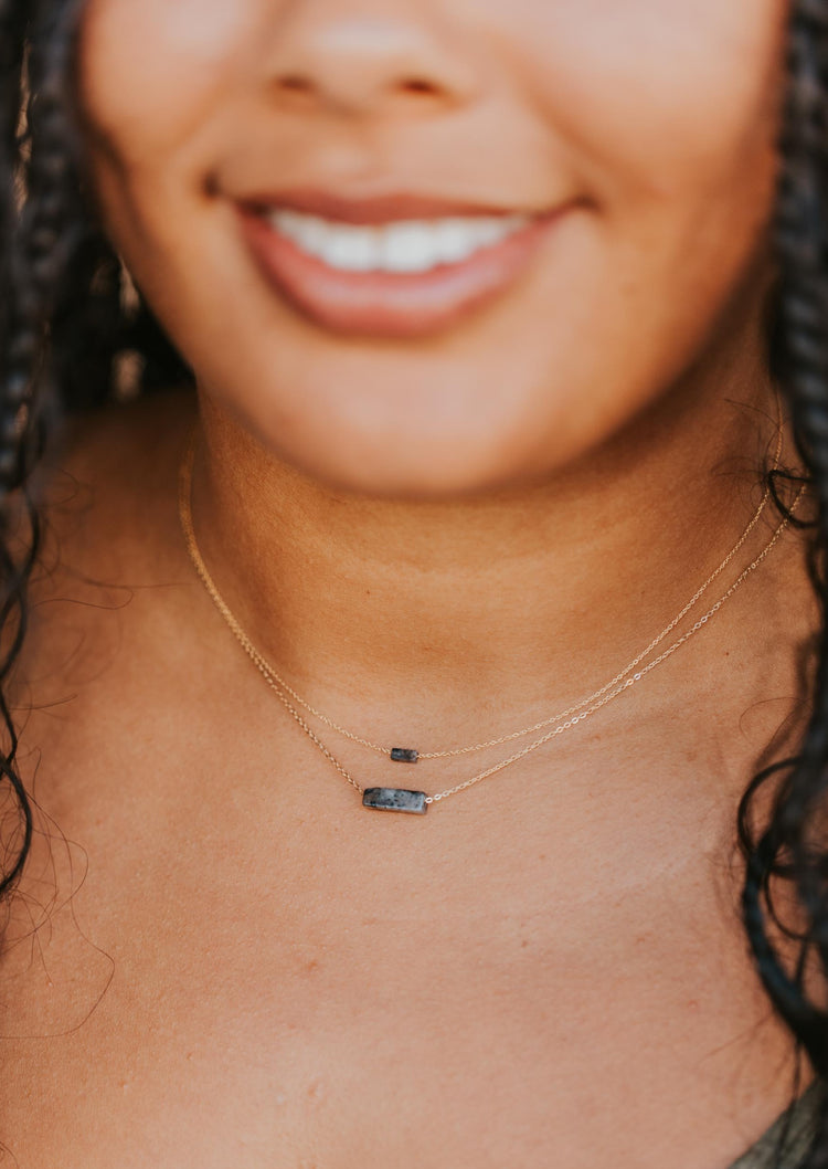 Two gemstone necklaces layered, part of the gemstone jewelry collection from Hello Adorn, a stone necklace with a labradorite black stone attached to a gold chain.