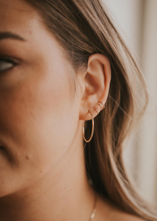 Everyday gold hoop earring shown styled in an ear with tiny hoop earrings and twist earrings in 14k gold fill.