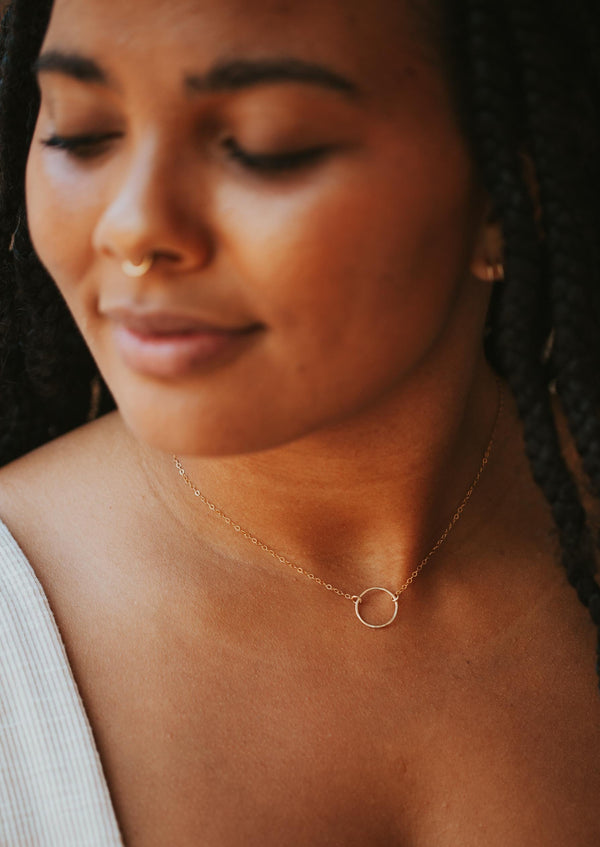 A model wearing a gold circle necklace from Hello Adorn in the Full Circle Necklace design, handmade jewelry using a circle pendant and gold chain necklace.
