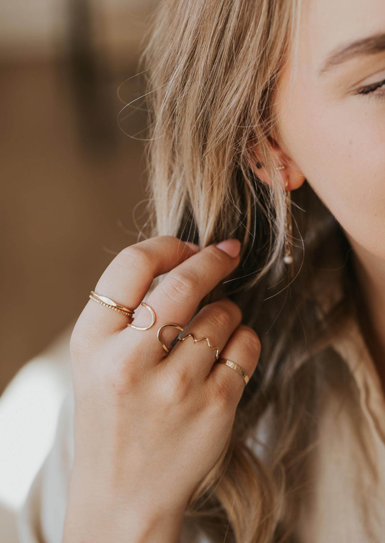 A gold ring stack styled by Hello Adorn using a beaded ring, a squiggle ring, a textured ring, and an open ring in Revolve Ring style.