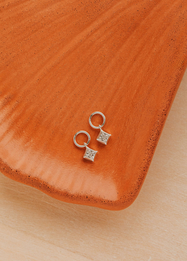 Sterling Silver Grace Charms by Hello Adorn - pair of CZ star charms on small silver huggies on ceramic dish