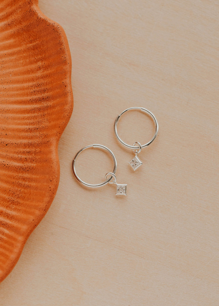 Sterling Silver Grace Hoops by Hello Adorn - pair of silver huggies with CZ star charms on ceramic prop