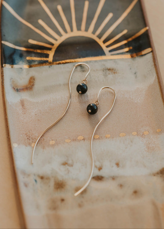 Gold threader earrings with black stones on a textured surface