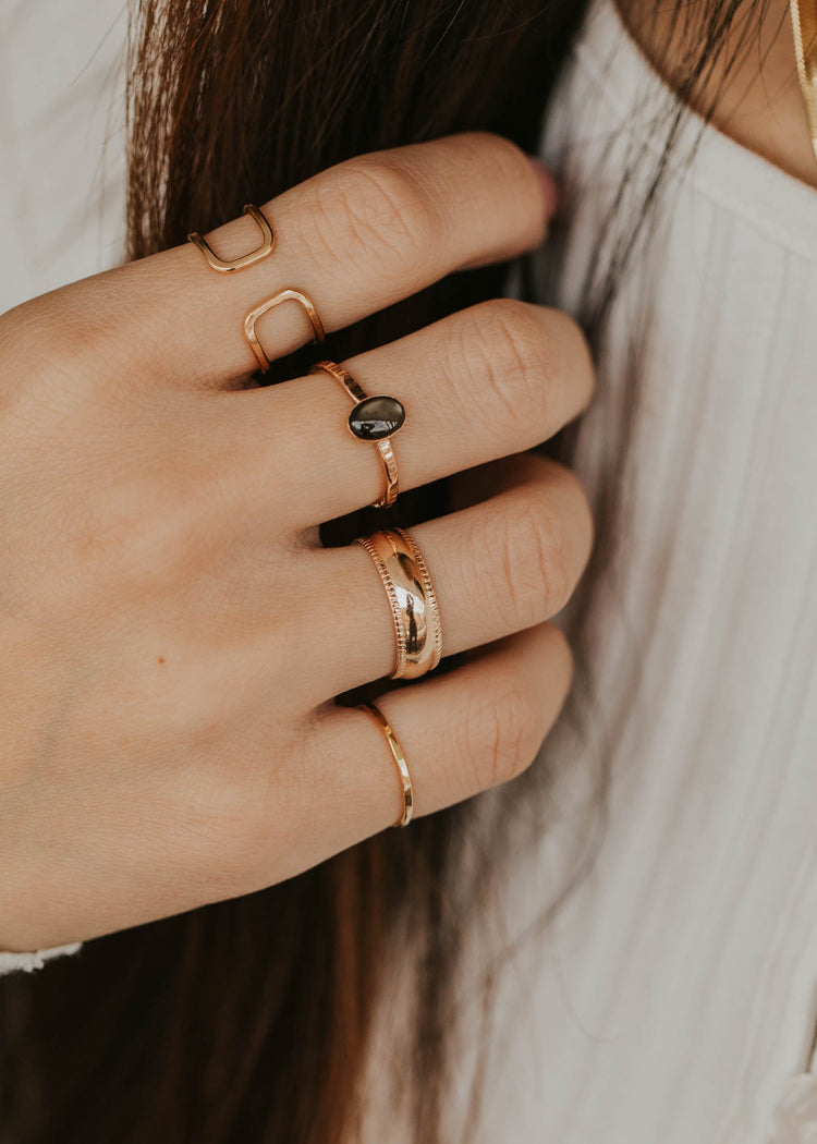 Close-up of a hand wearing multiple gold rings with a blurred background