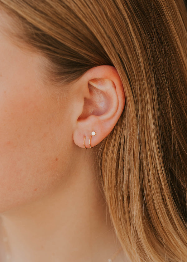 Close-up of an ear wearing a small earring with blonde hair.