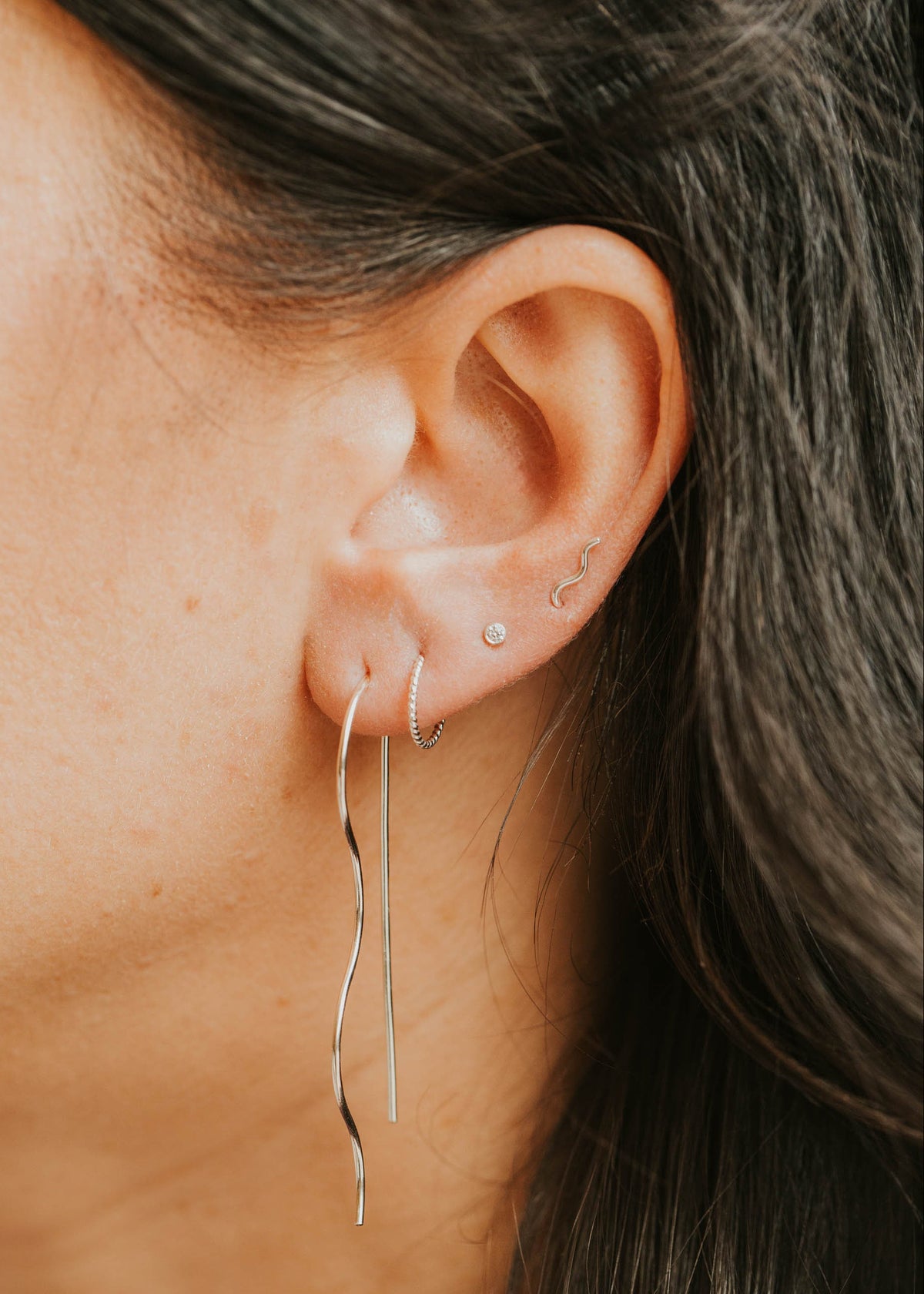 Close-up of an ear with multiple earrings against a blurred background
