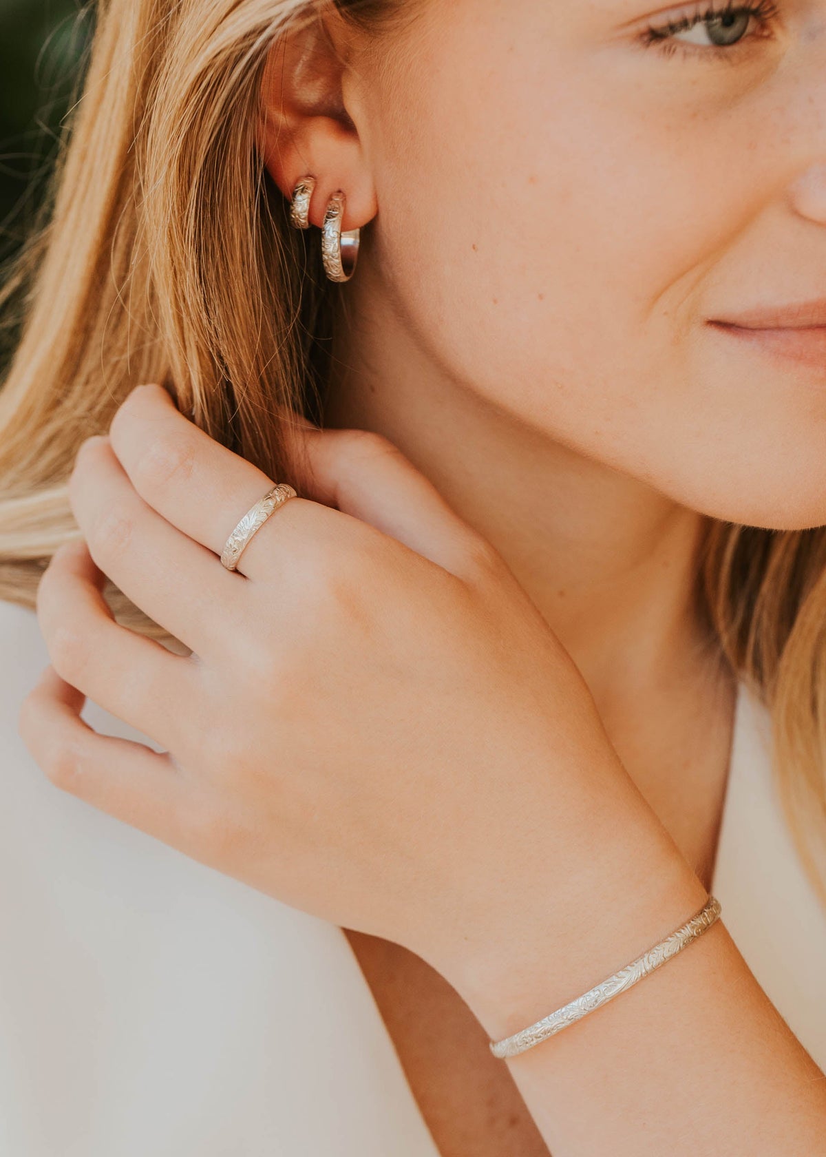 Close-up of a woman wearing silver hoop earrings, ring, and bracelet.