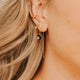 Close-up of a person wearing gold threader earrings with a black stone and a blurred background