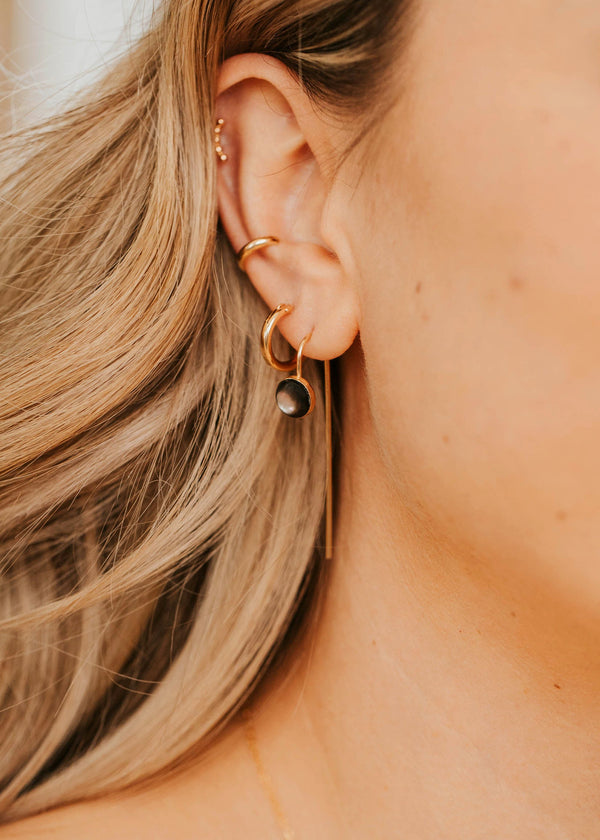 Close-up of a person wearing gold threader earrings with a black stone and a blurred background