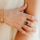 Close-up of a hand wearing gold rings and bracelets on a neutral background
