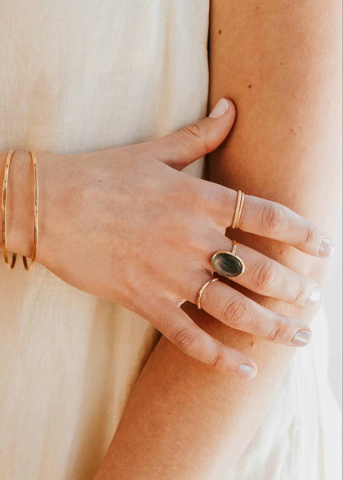 Close-up of a hand wearing gold rings and bracelets on a neutral background