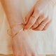 Close-up of hands wearing gold bracelets and rings on a neutral background