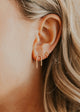 Close-up of an ear with gold earrings against a neutral background