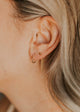 Close-up of an ear wearing gold hoop and chain earrings with blurred background