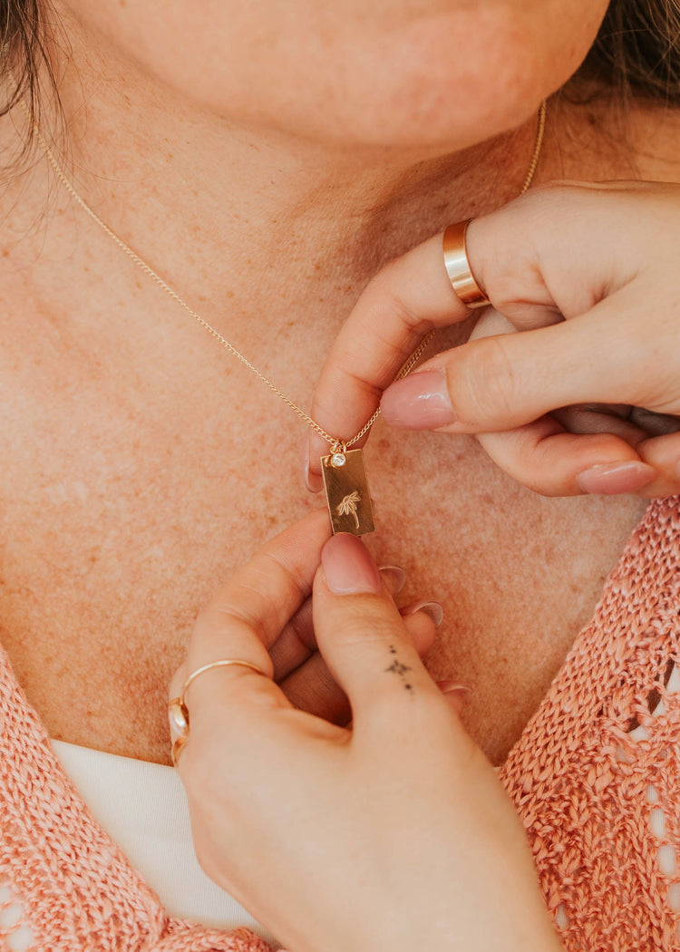 Close-up of a person adjusting a gold necklace on another person.