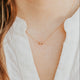 Close-up of a person wearing a delicate gold necklace with a small pendant against a blurred background.