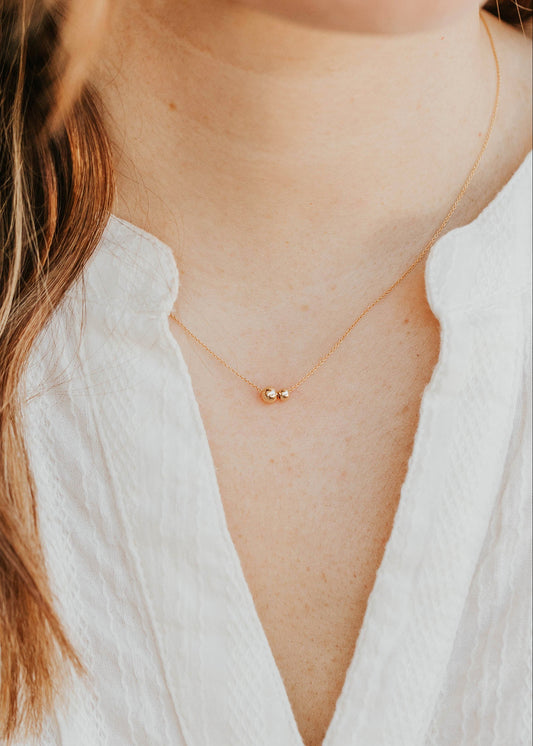 Close-up of a person wearing a delicate gold necklace with a small pendant against a blurred background.