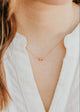 Close-up of a person wearing a delicate gold necklace with a small pendant against a blurred background.