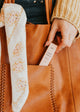 Person holding a brown leather bag with a white floral scarf and a product labeled 'Cacao Panna' inside.