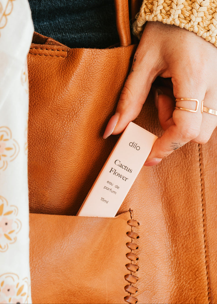 Person holding a small pink box labeled 'dilo' next to a brown leather bag.