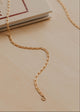 Gold chain necklace on a beige surface with a book in the background