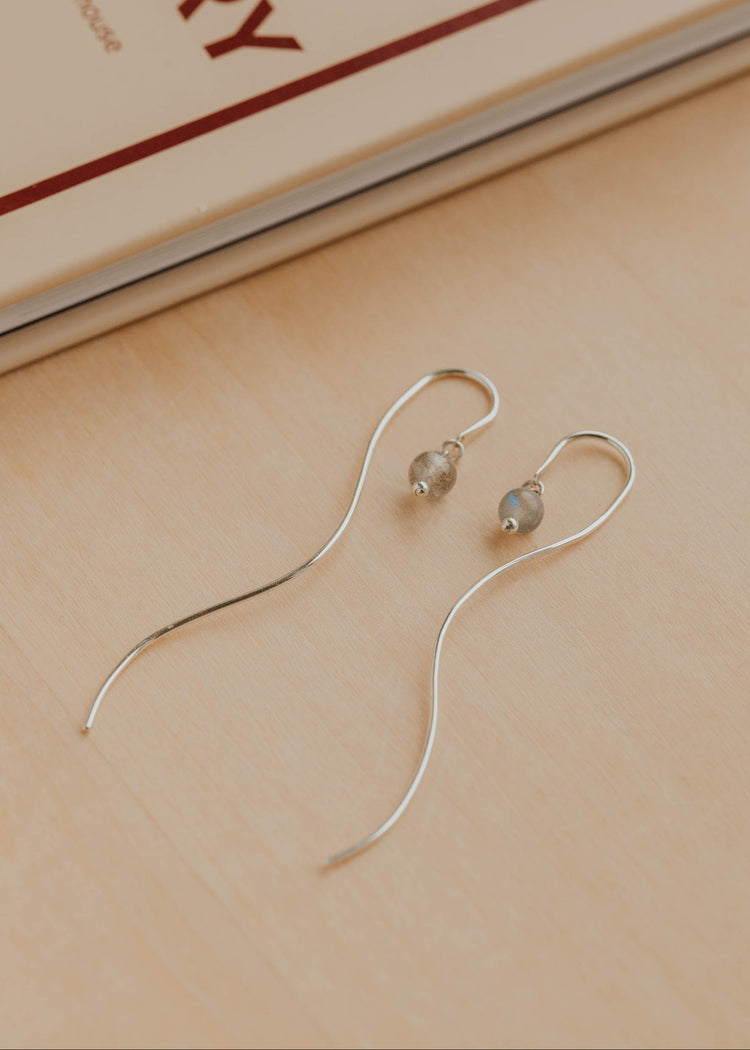 Silver earrings with small gemstones on a beige surface with a book in the background