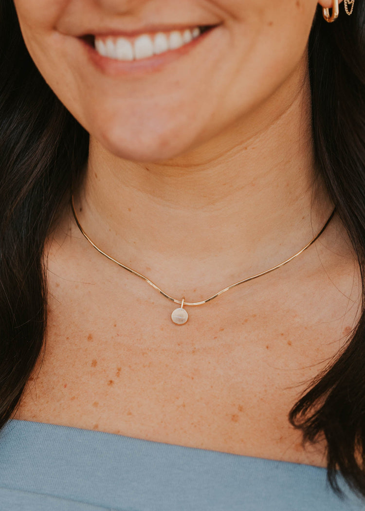 Close-up of a person wearing a delicate gold necklace with a small pendant.